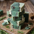 Stack of green soap bars with rosemary leaves on a wooden surface
